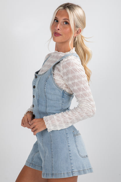 Woman wearing a denim dress over a white lace top on a light gray background