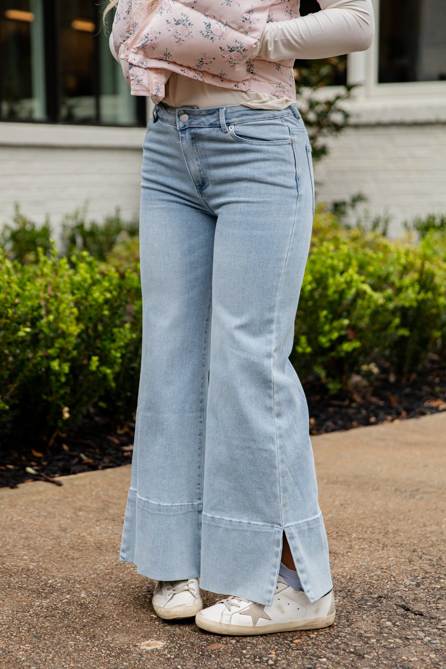 Person wearing light blue flared jeans standing outdoors with greenery in the background