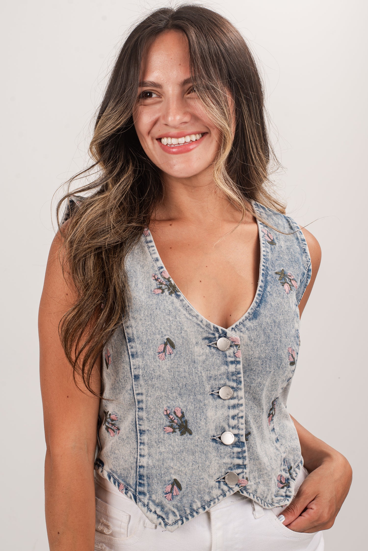 Woman wearing a denim vest with floral embroidery on a plain background