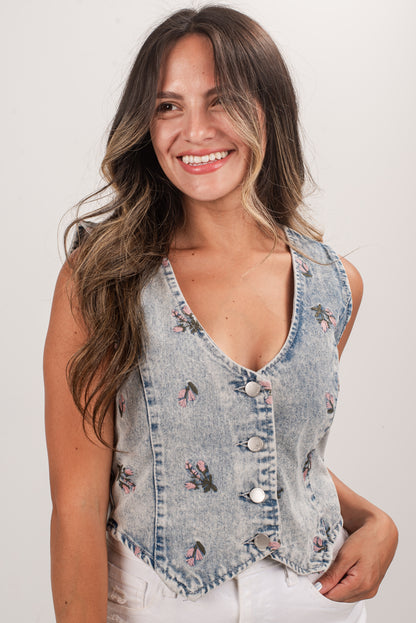 Woman wearing a denim vest with floral embroidery on a plain background