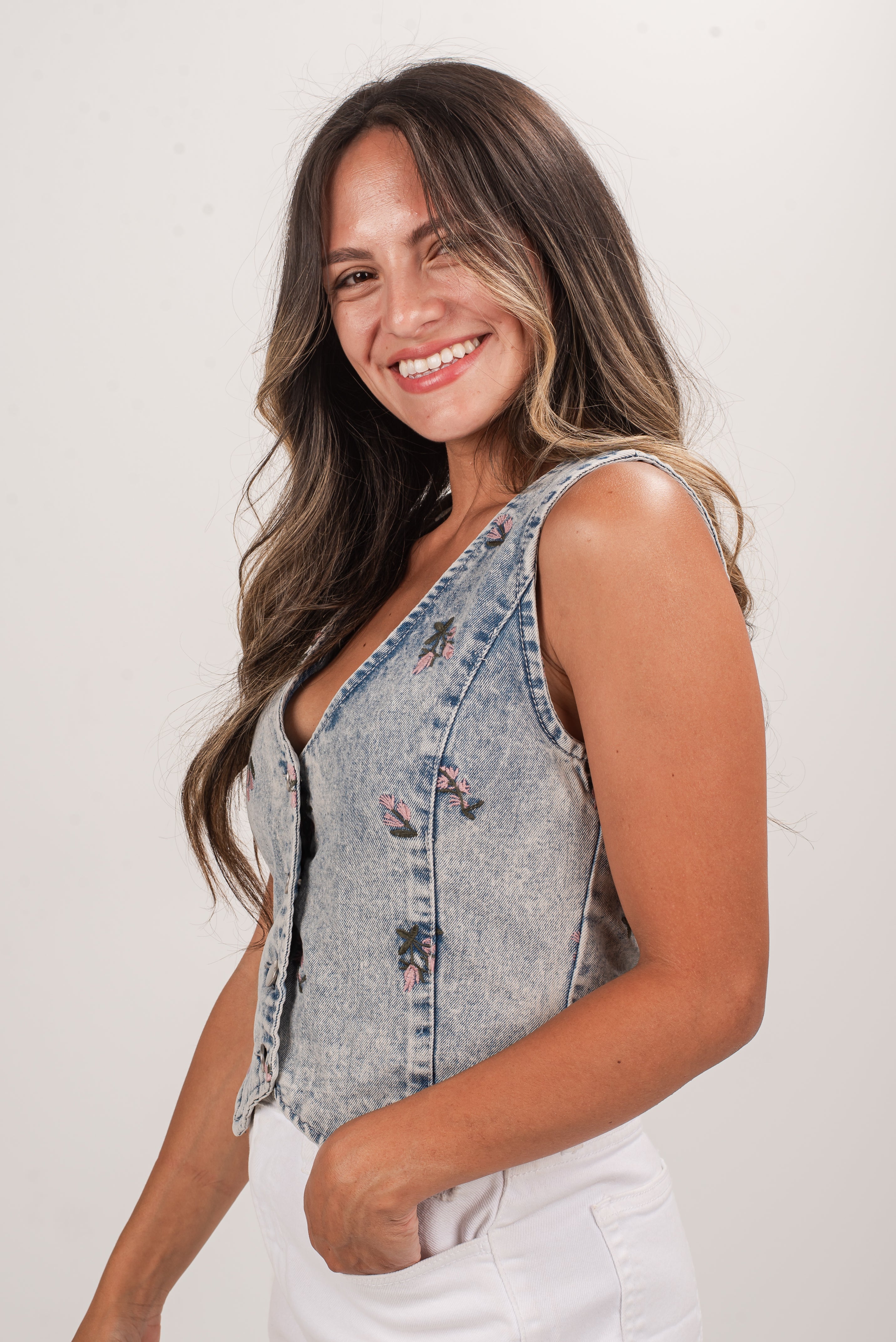 Woman wearing a denim vest with floral patterns on a plain background