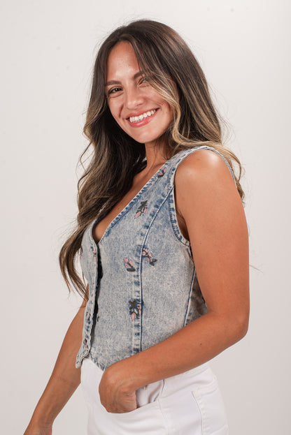 Woman wearing a denim vest with floral patterns on a plain background