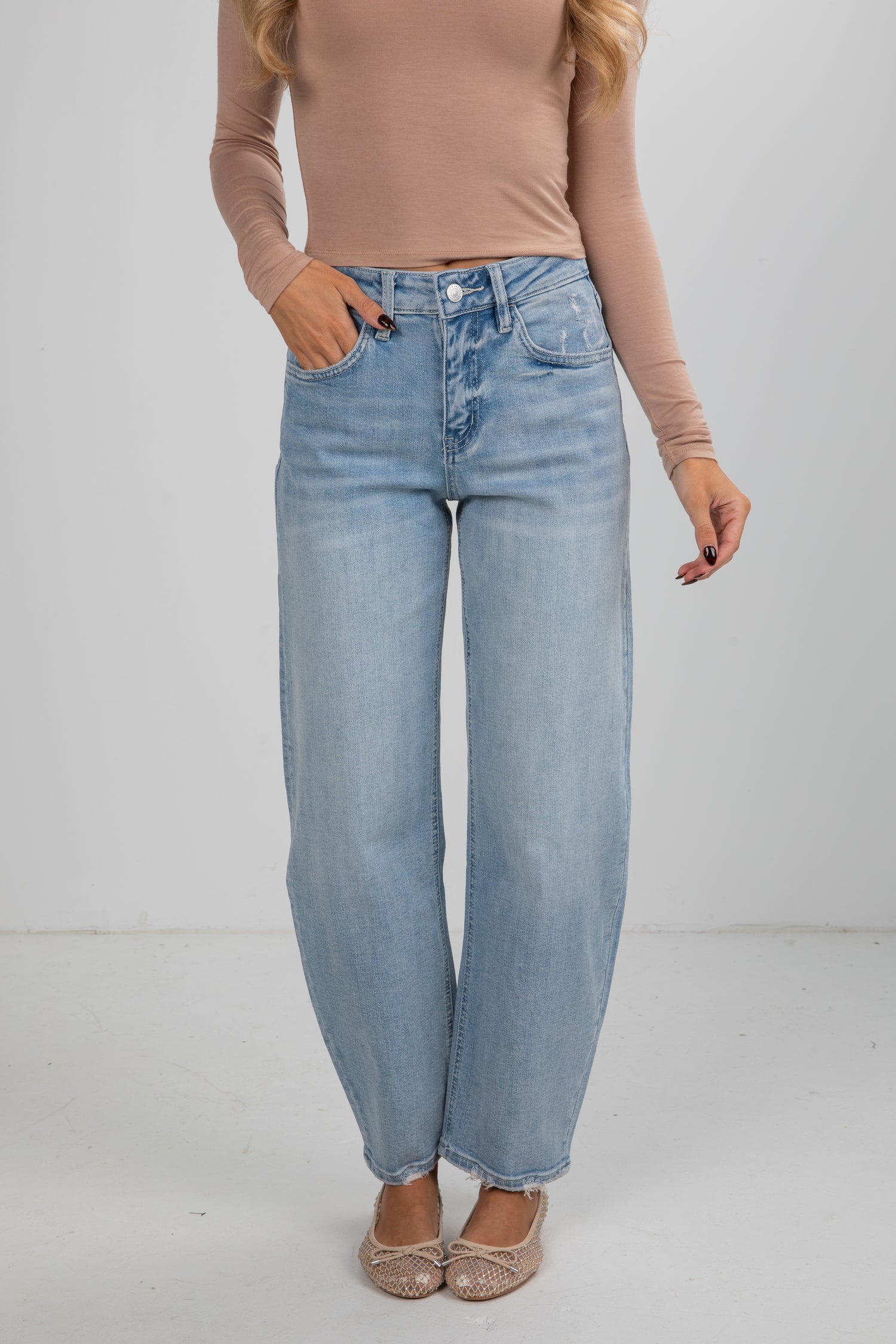 Person wearing light blue jeans and a beige top on a plain background