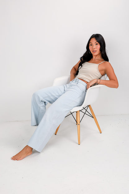 Woman sitting on a chair wearing light blue jeans and a beige top against a white background
