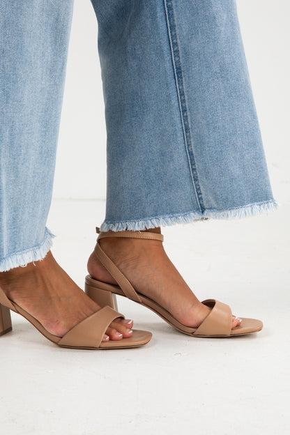 Tan high-heeled sandals worn with light blue jeans on a white background