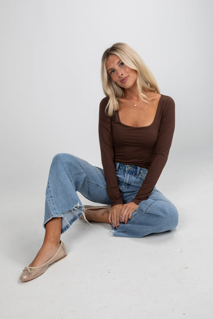 Woman wearing a brown top and blue jeans sitting on a white background