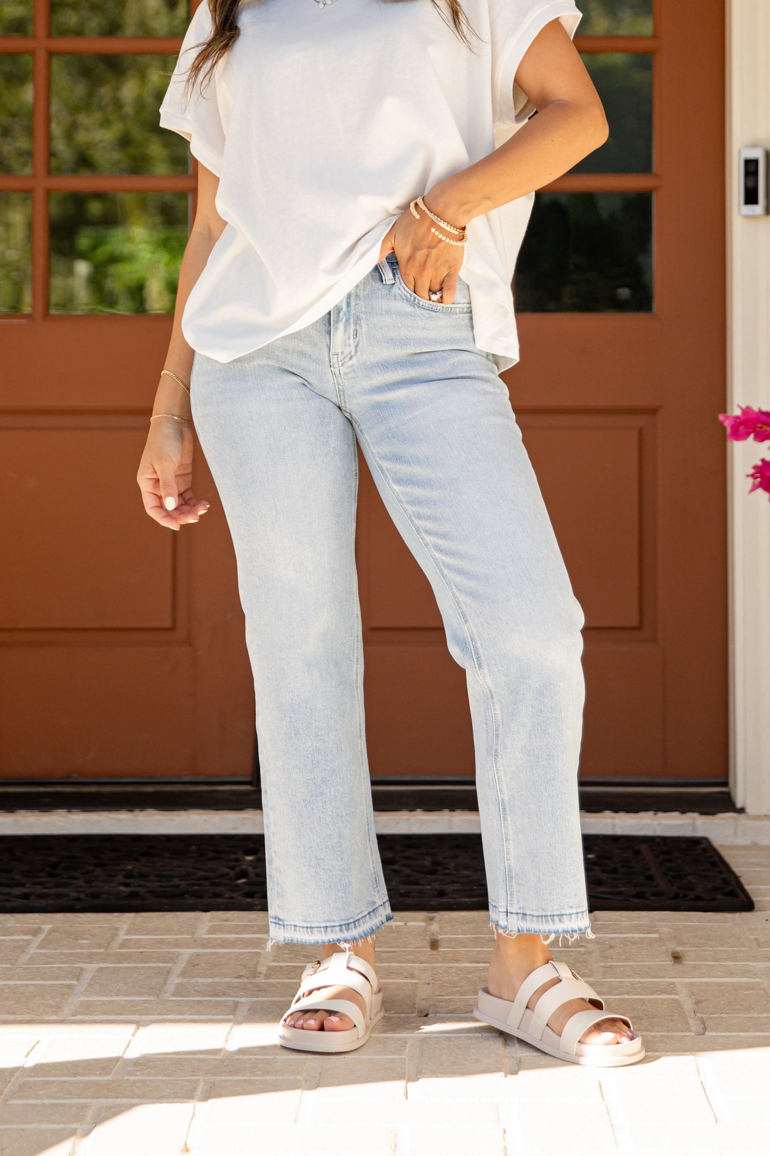 Person wearing light blue jeans and a white shirt standing on a porch.