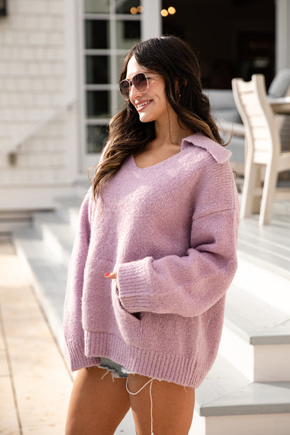 Woman wearing a pink sweater standing outdoors on a patio.