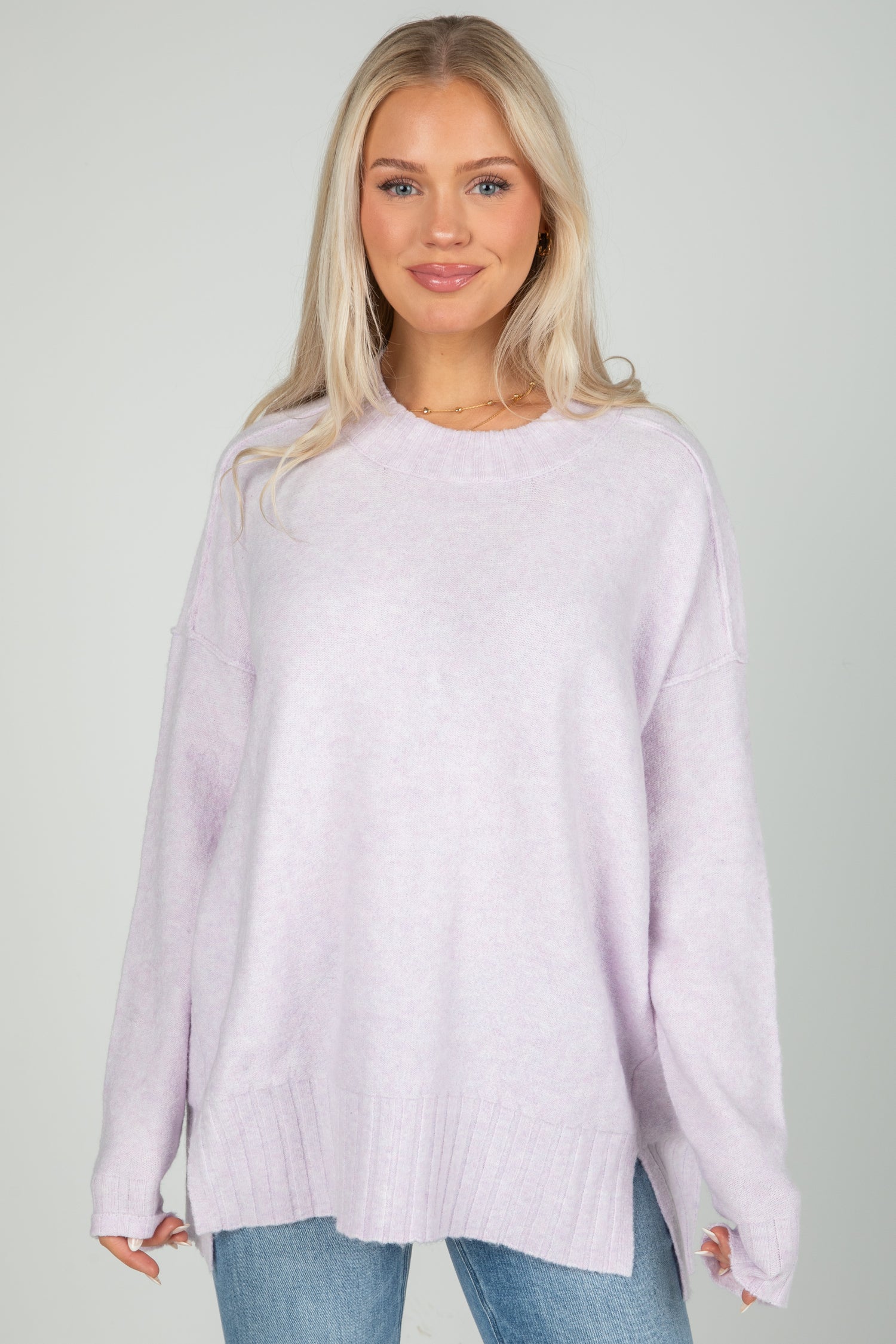 Woman wearing a light purple sweater and blue jeans against a plain background