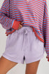 Person wearing a red and blue striped shirt with a drawstring purple shorts on a plain background