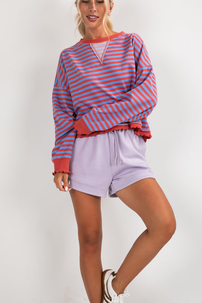 Person wearing a red and blue striped sweater with purple shorts on a white background