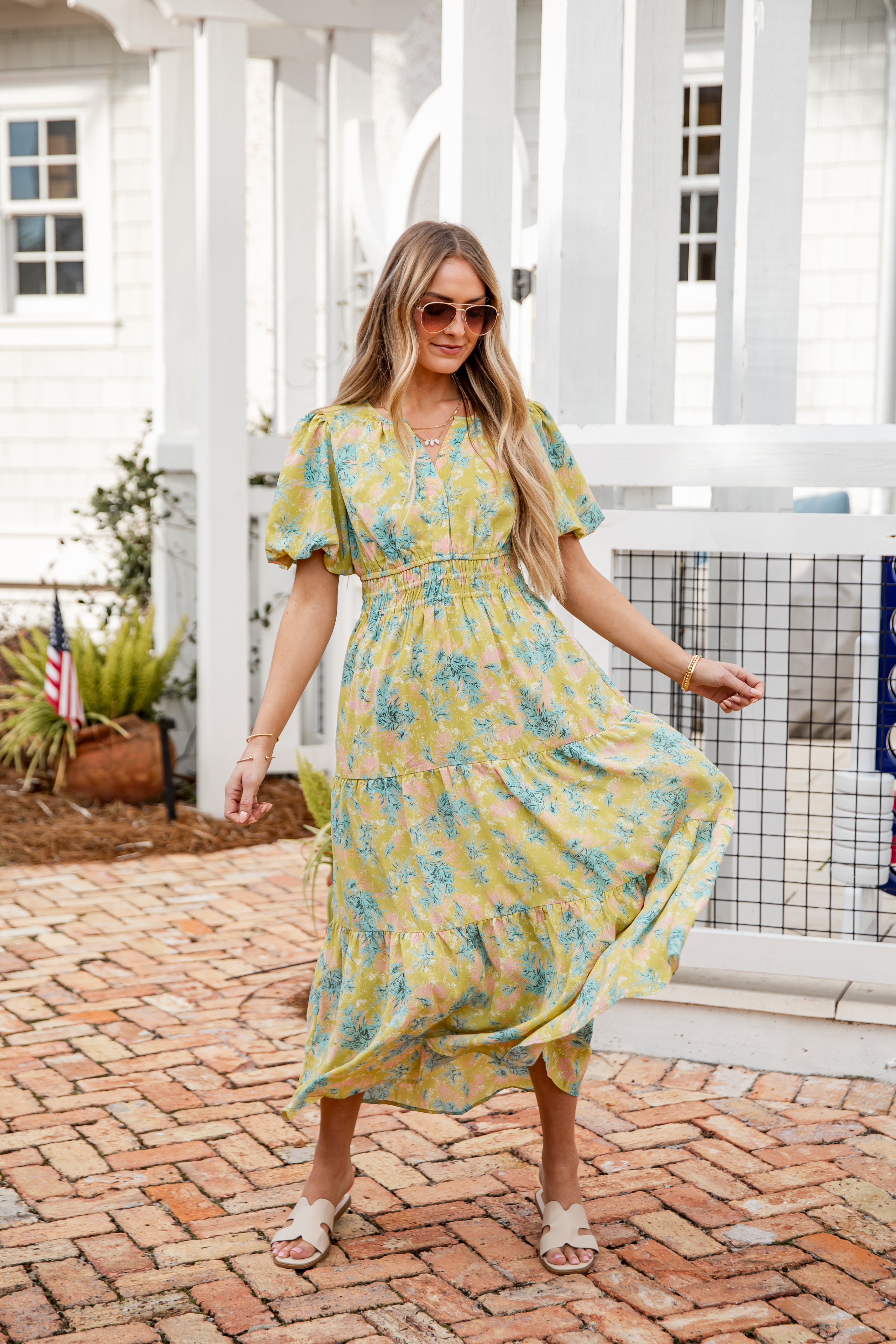 Woman in a yellow floral dress standing on a brick patio.