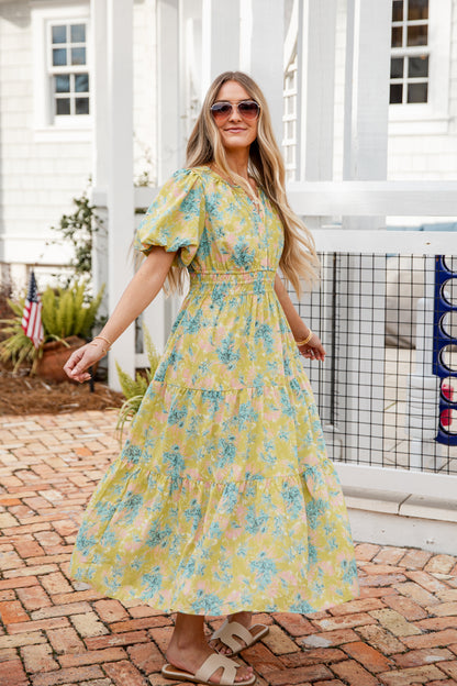 Woman wearing a yellow floral dress standing on a brick patio.