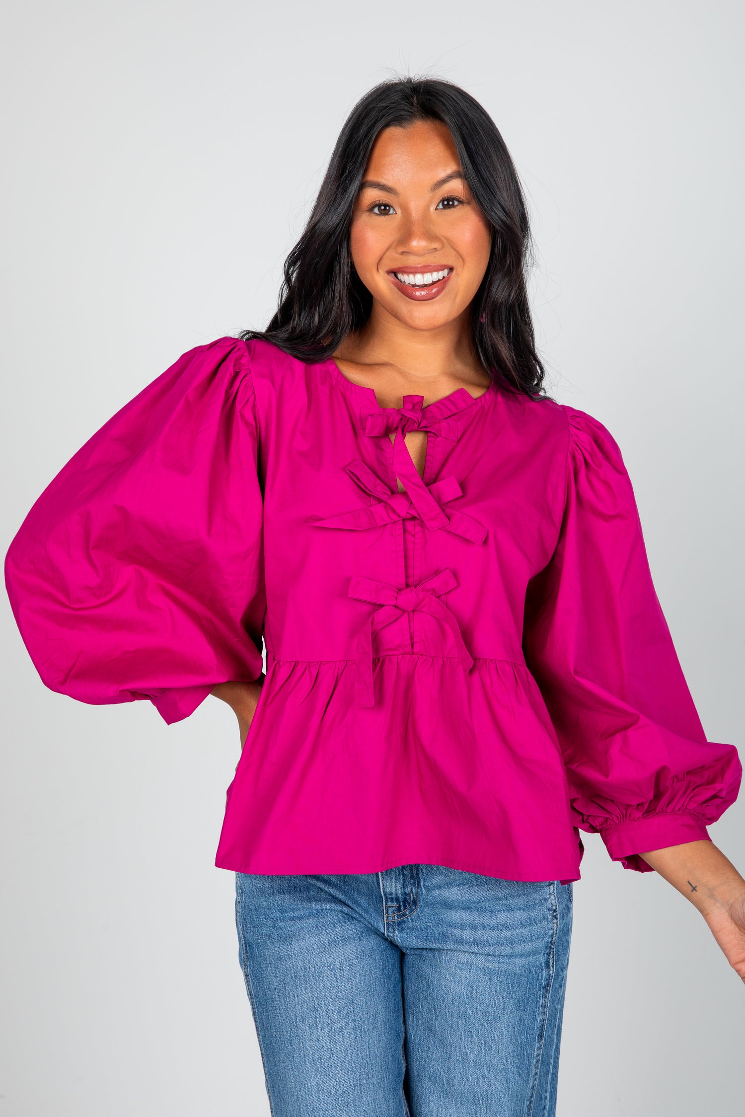 Woman wearing a bright pink blouse with puffed sleeves on a plain background