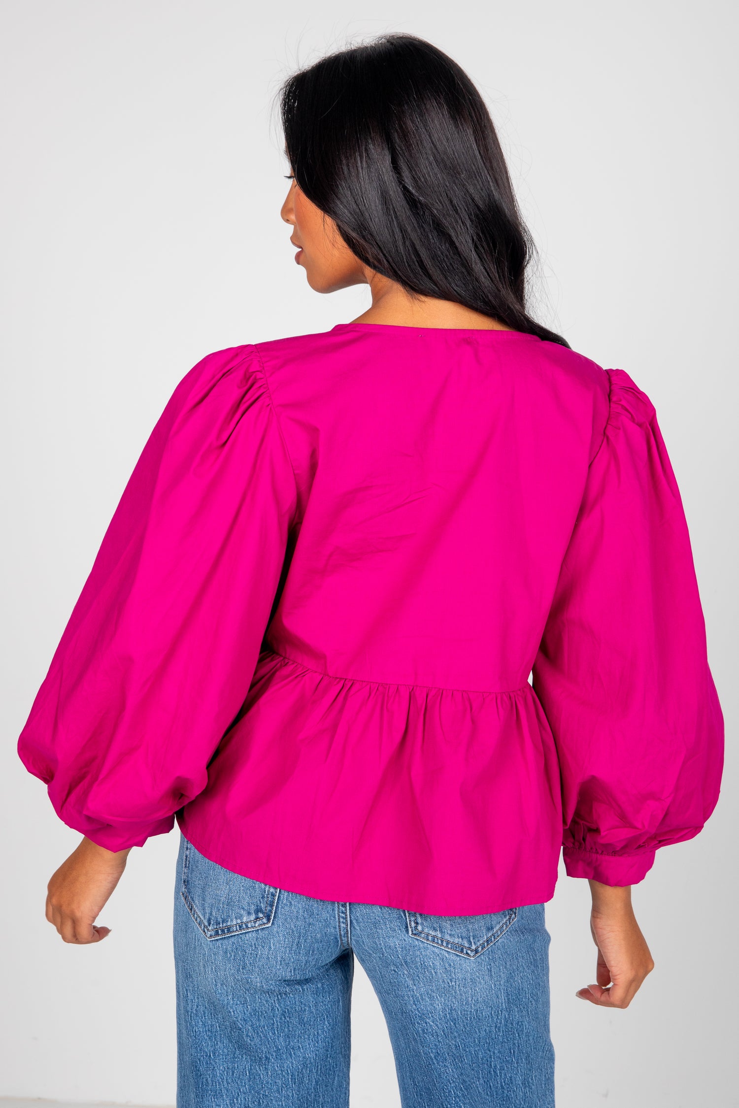 Person wearing a bright pink blouse with puffed sleeves and blue jeans on a white background
