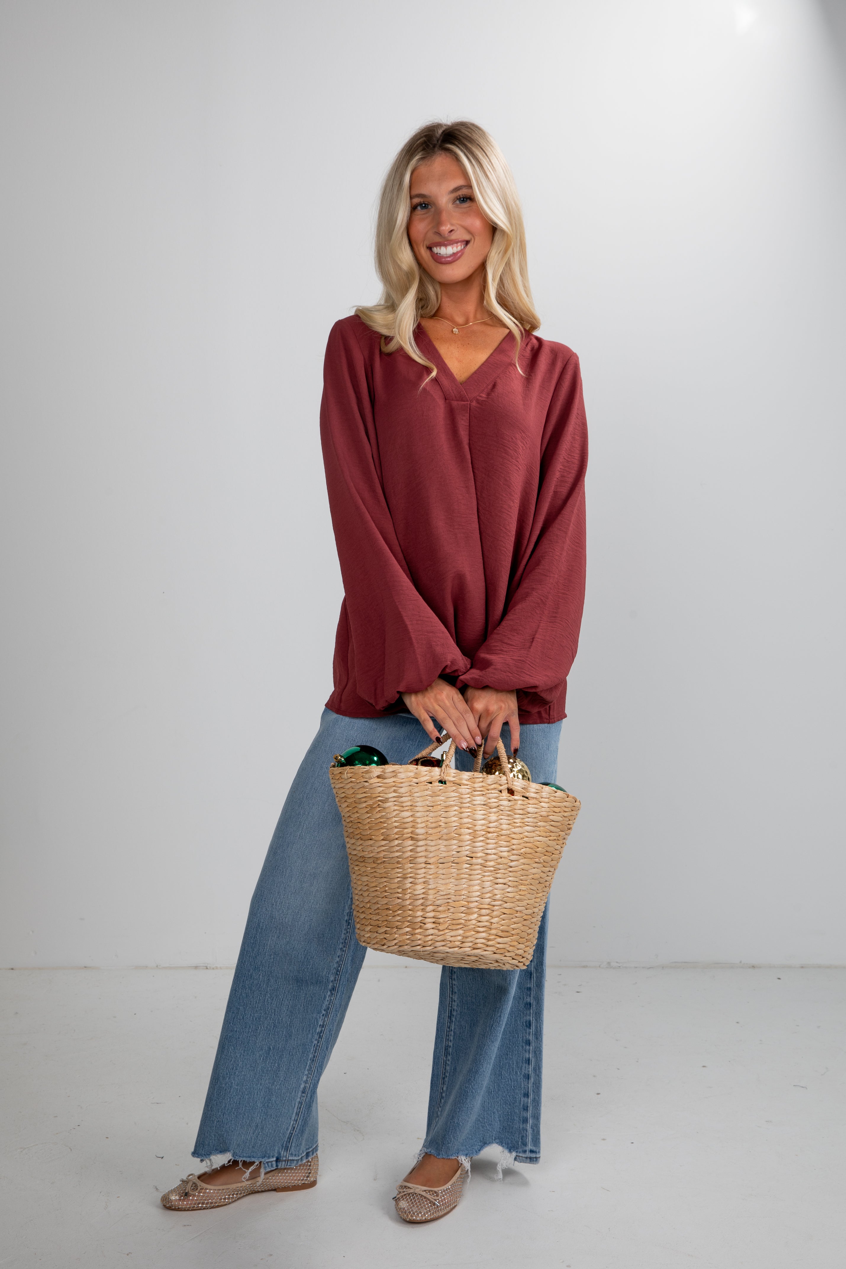 Woman holding a woven basket wearing a red sweater and blue jeans on a white background