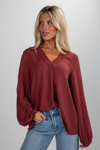 Woman wearing a burgundy blouse and blue jeans on a plain background