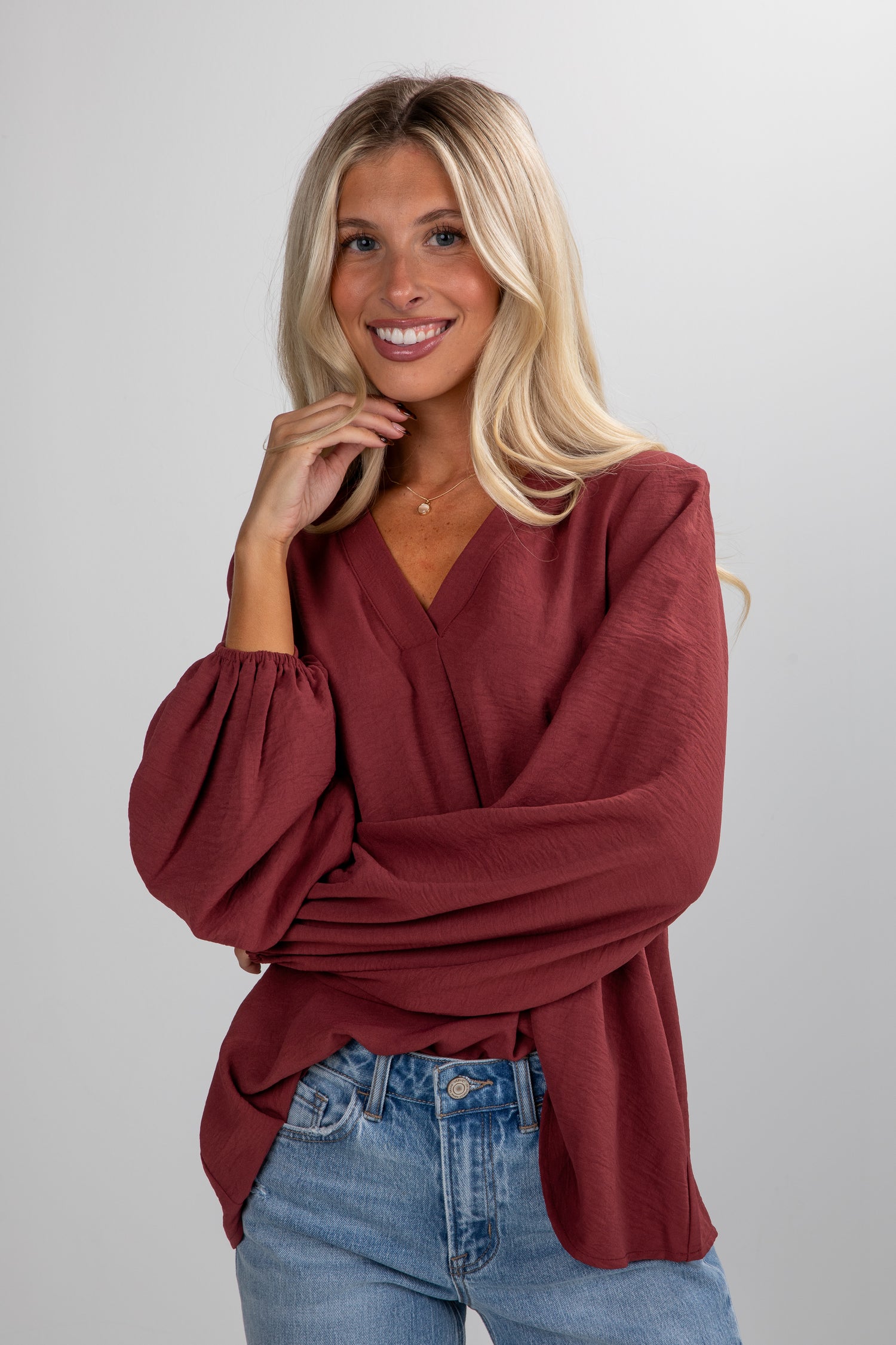 Woman wearing a burgundy top and blue jeans on a plain background