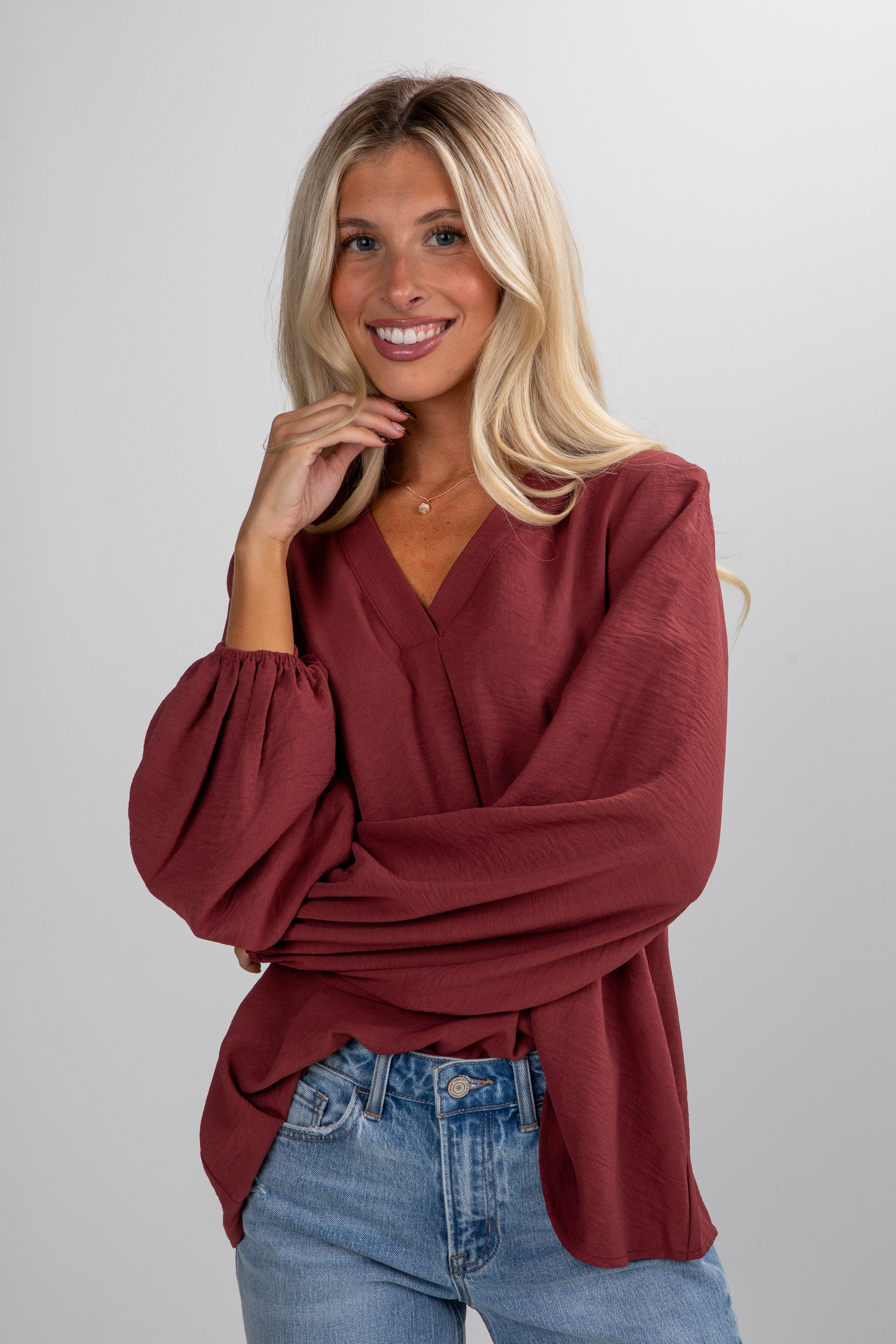 Woman wearing a burgundy top and blue jeans on a plain background