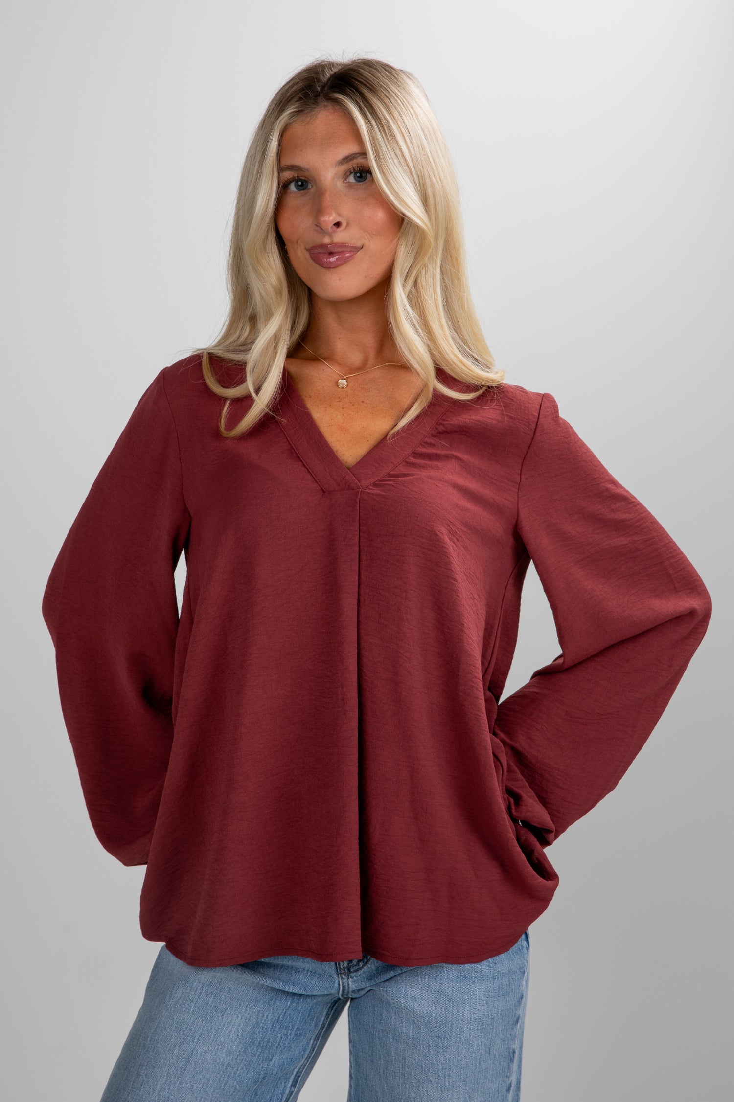 Woman wearing a burgundy blouse and blue jeans against a plain background