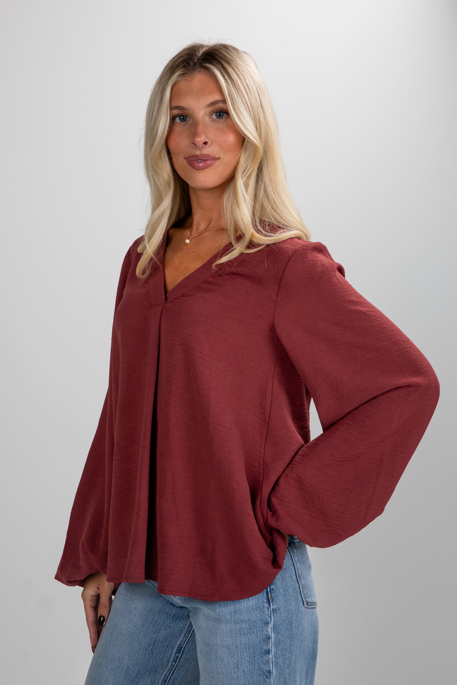 Woman wearing a burgundy top and blue jeans against a plain background