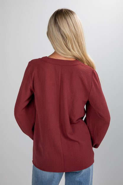 Person wearing a burgundy sweater and blue jeans on a plain background