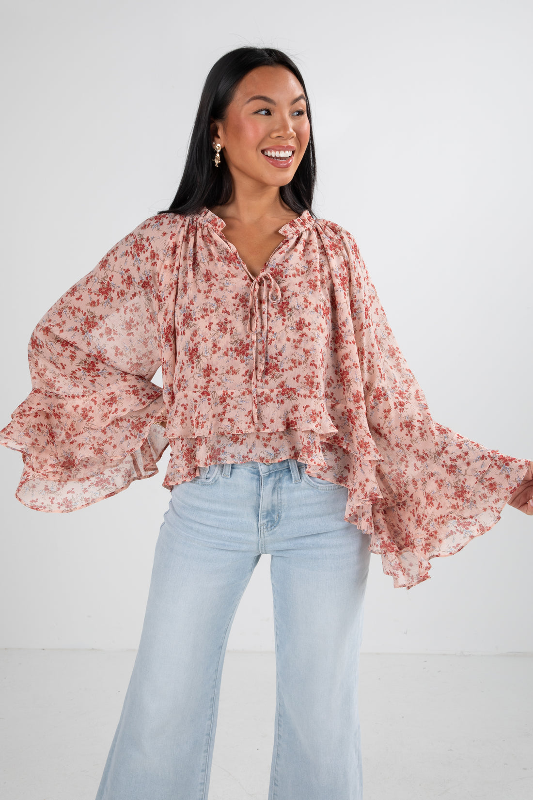 Woman wearing a floral blouse and light blue jeans against a white background