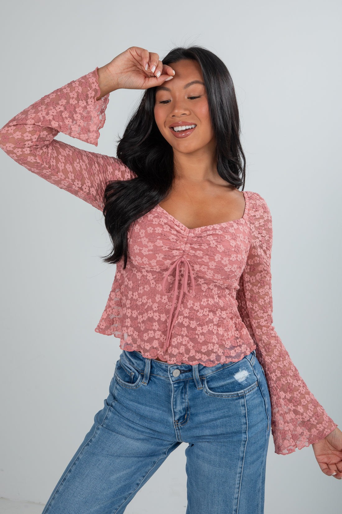 Woman wearing a pink floral long-sleeve top and blue jeans against a gray background