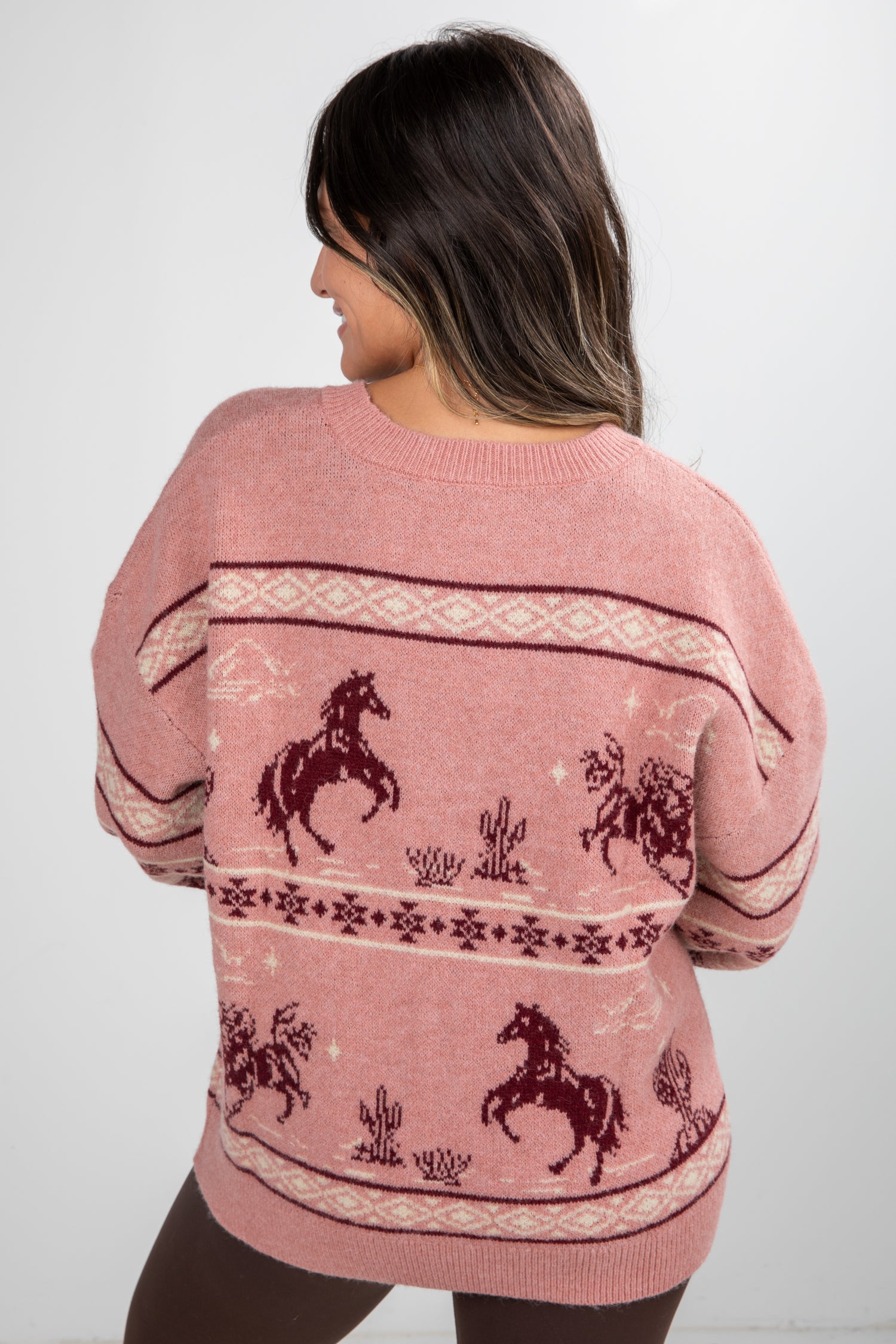 Person wearing a pink sweater with horse patterns on a white background