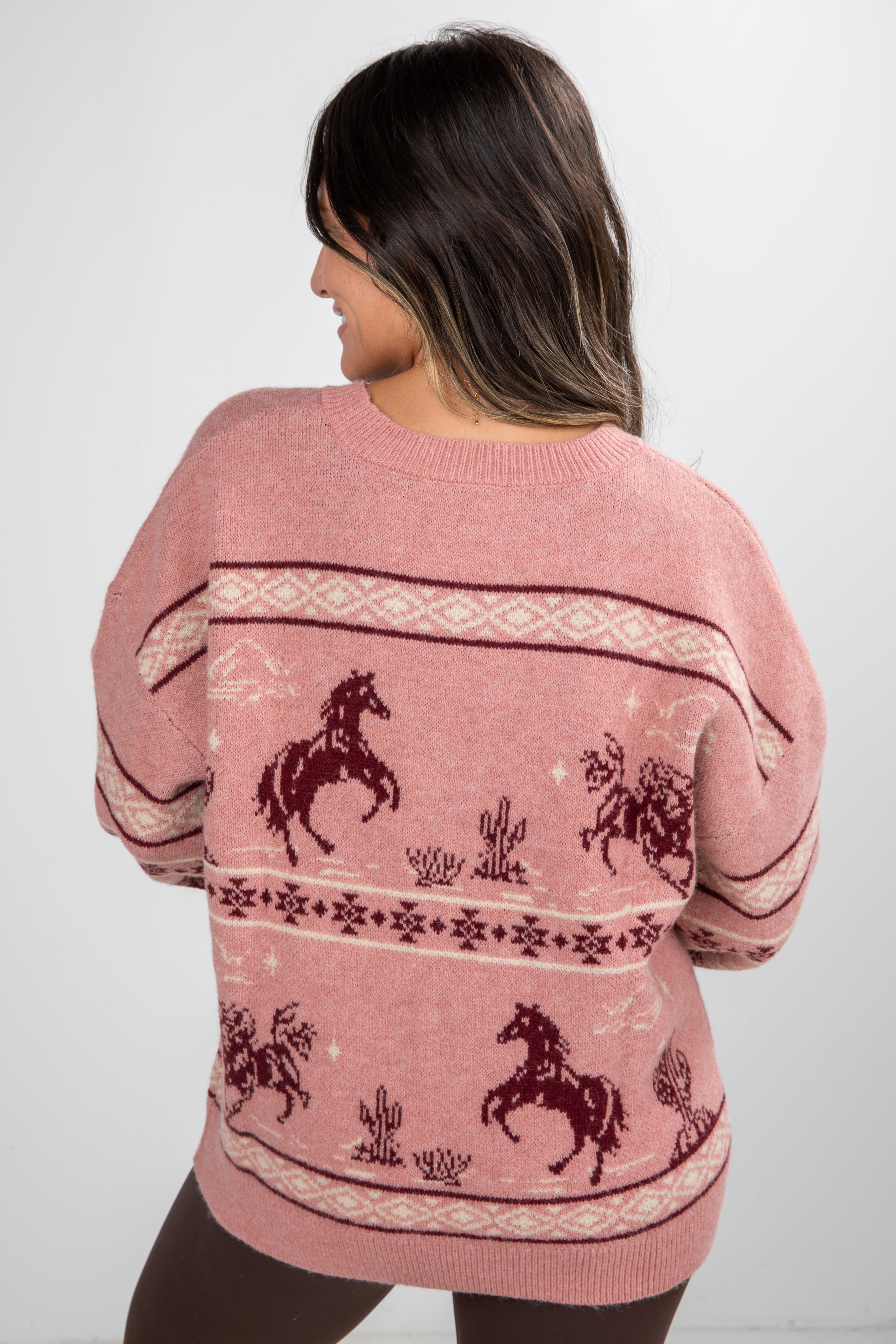 Person wearing a pink sweater with horse patterns on a white background