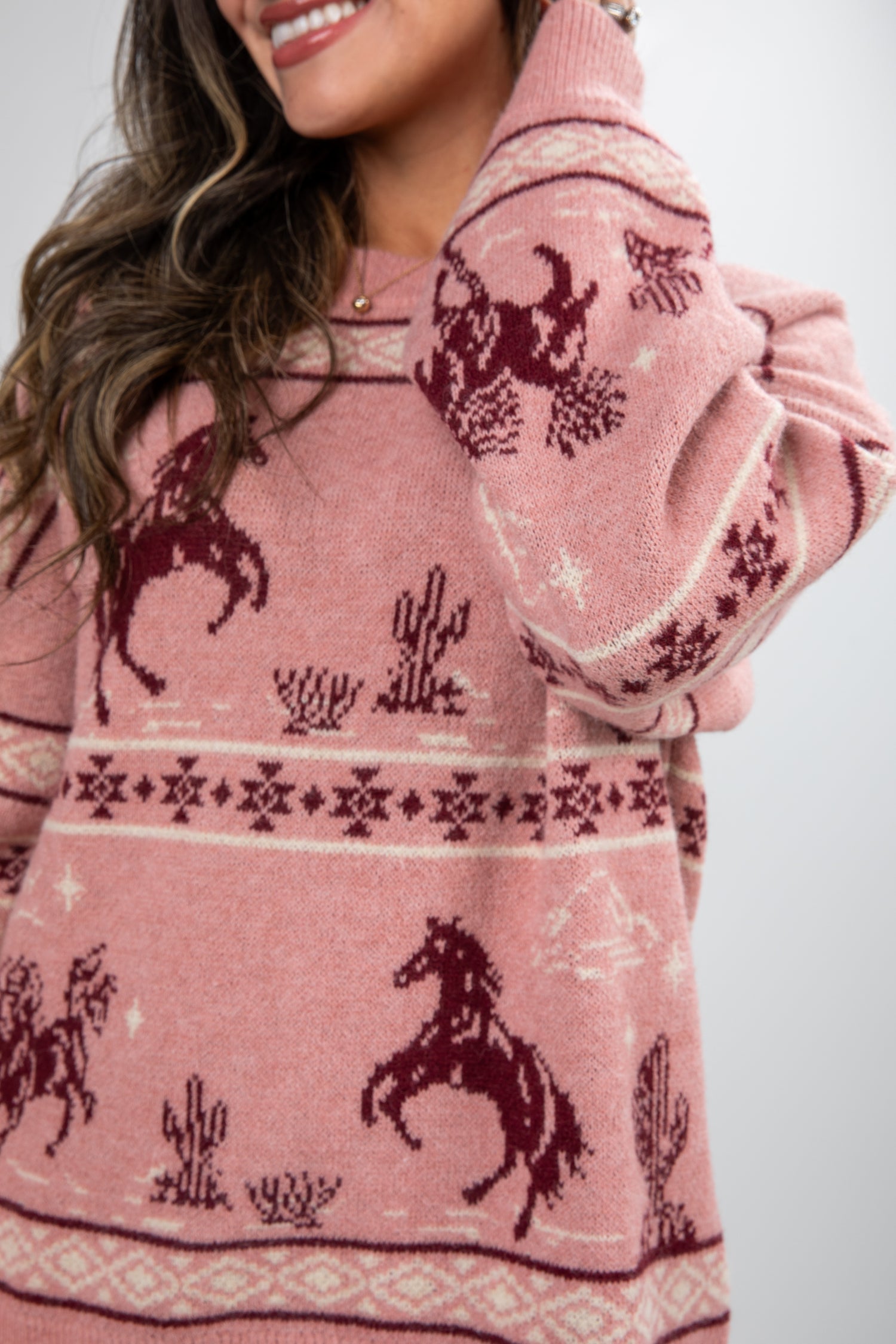 Person wearing a pink sweater with horse and cactus patterns on a white background