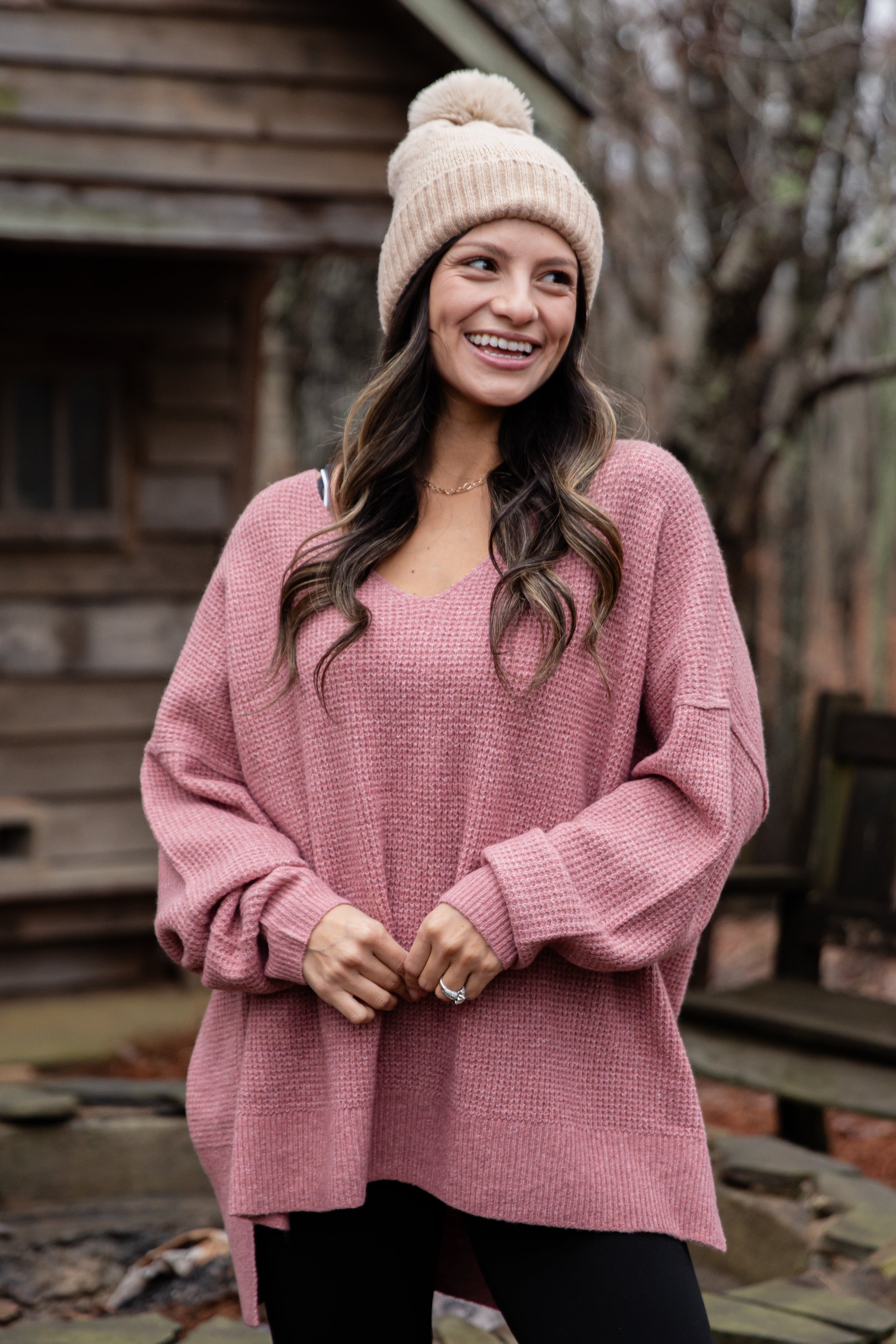 Woman wearing a pink sweater and knit hat outdoors.