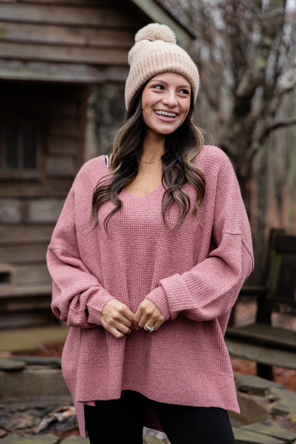 Woman wearing a pink sweater and knit hat outdoors.