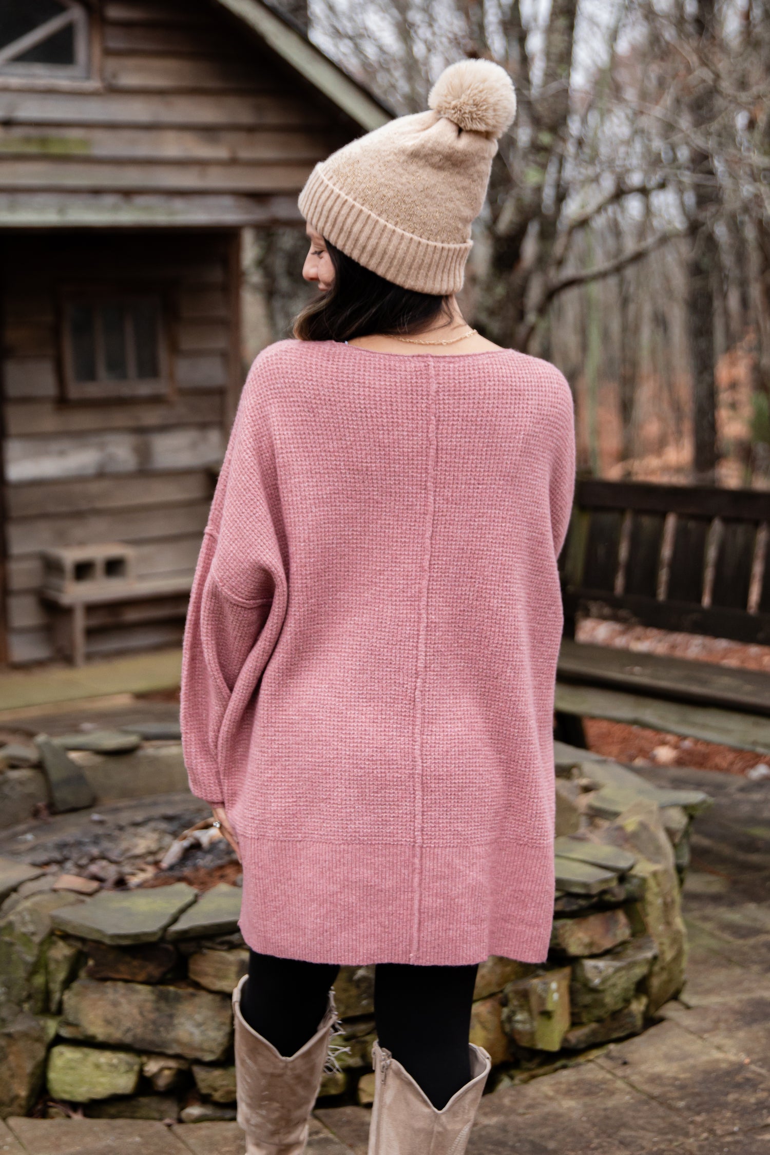 Person wearing a pink sweater and beige beanie in a rustic outdoor setting.