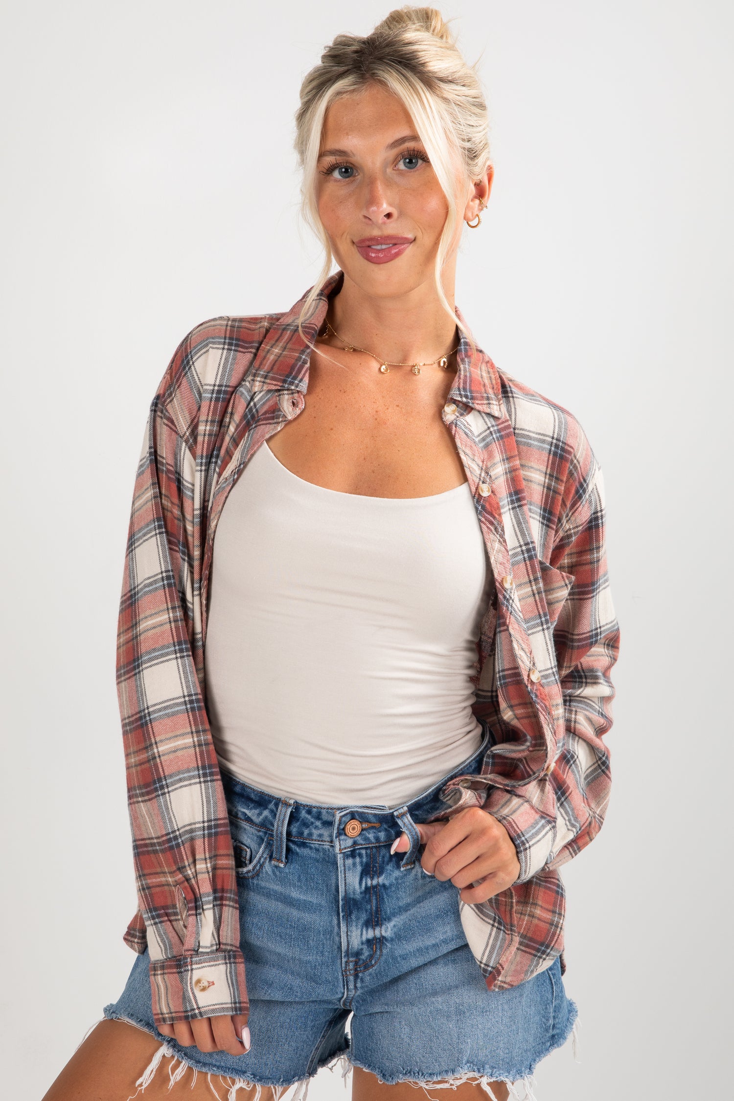 Woman wearing a plaid shirt over a white tank top and denim shorts on a white background