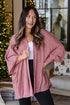 Woman wearing a pink cardigan in a cozy living room with Christmas decorations.