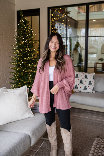 Woman in a pink cardigan standing in a living room with a Christmas tree.