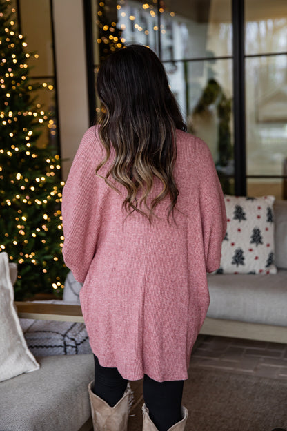 Person wearing a pink sweater standing in a cozy living room with Christmas decorations.