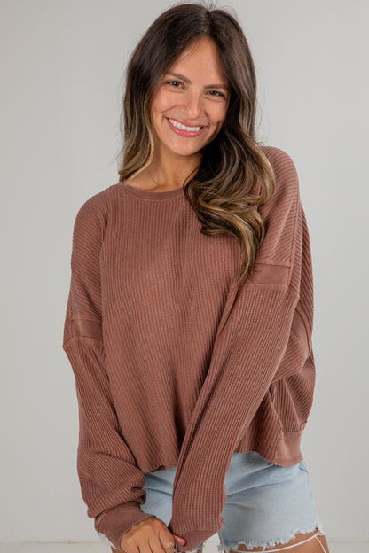 Woman wearing a brown ribbed sweater and light blue jeans against a plain background
