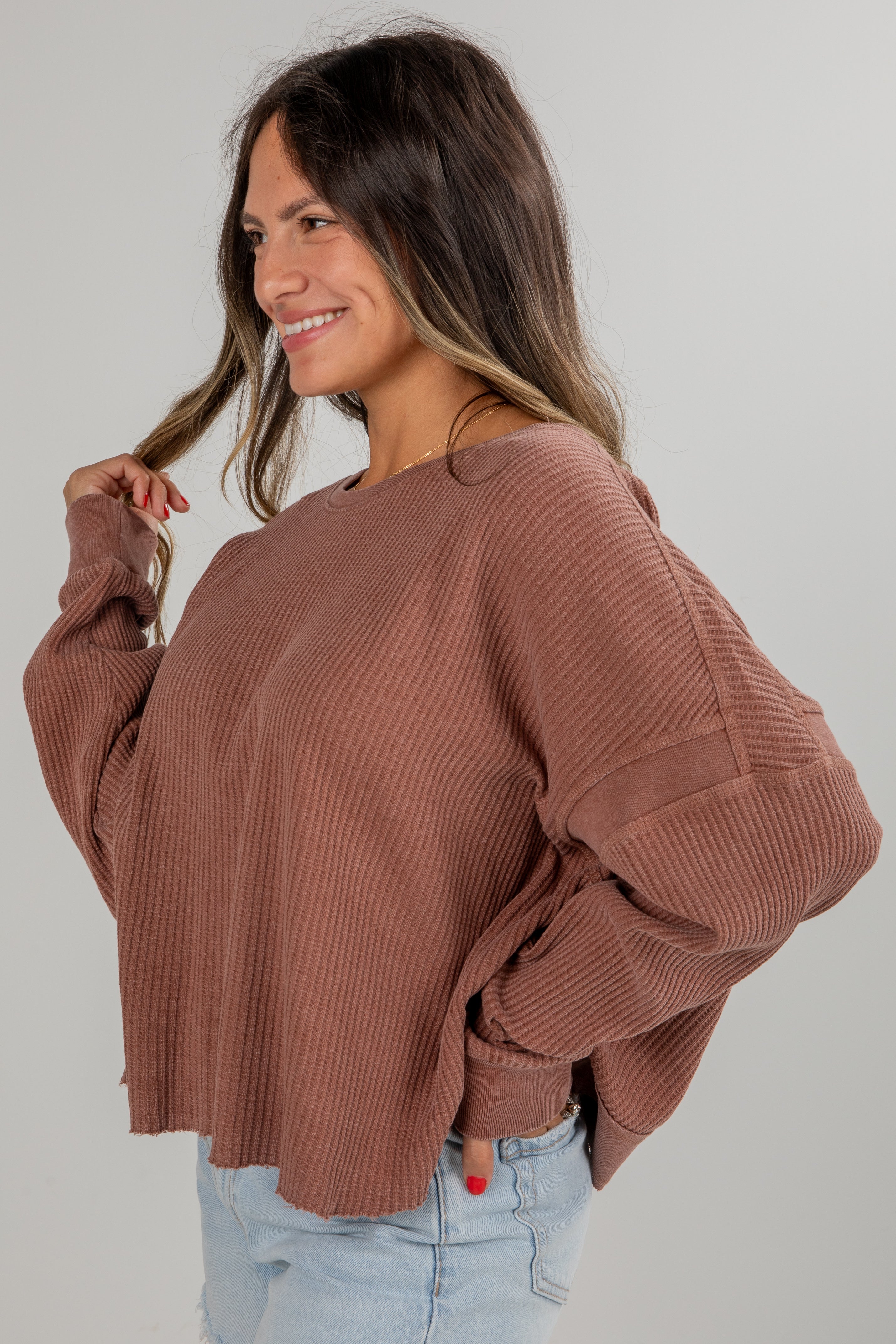 Woman wearing a brown sweater and light blue jeans against a plain background