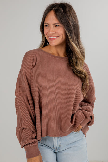 Woman wearing a brown ribbed sweater and light blue jeans against a plain background