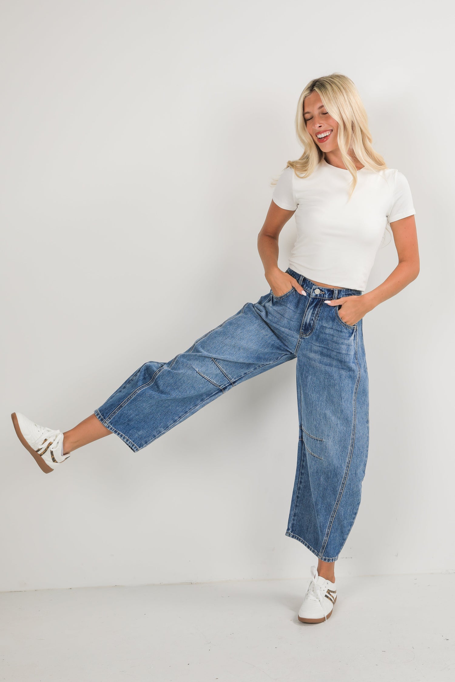Woman wearing a white top and blue jeans posing against a plain background