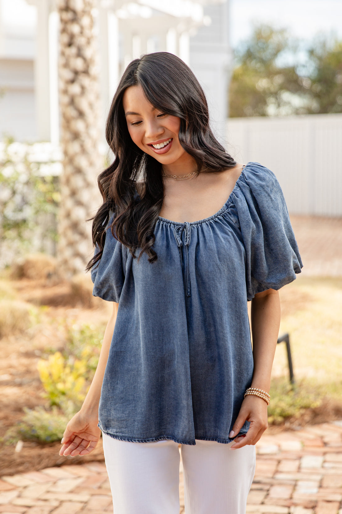 Woman wearing a blue off-shoulder top and white pants outdoors.