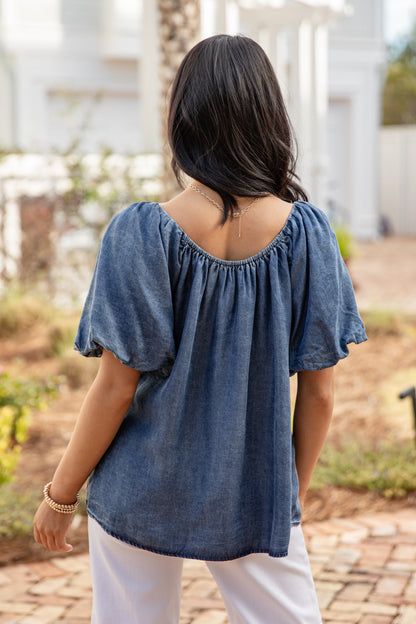 Woman wearing a blue top and white pants standing outdoors.