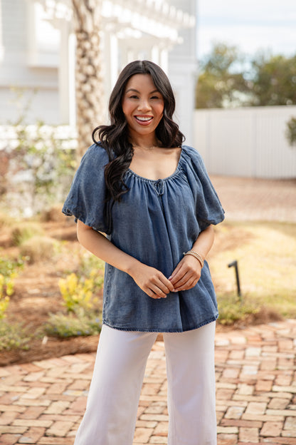 Woman wearing a blue top and white pants standing outdoors.