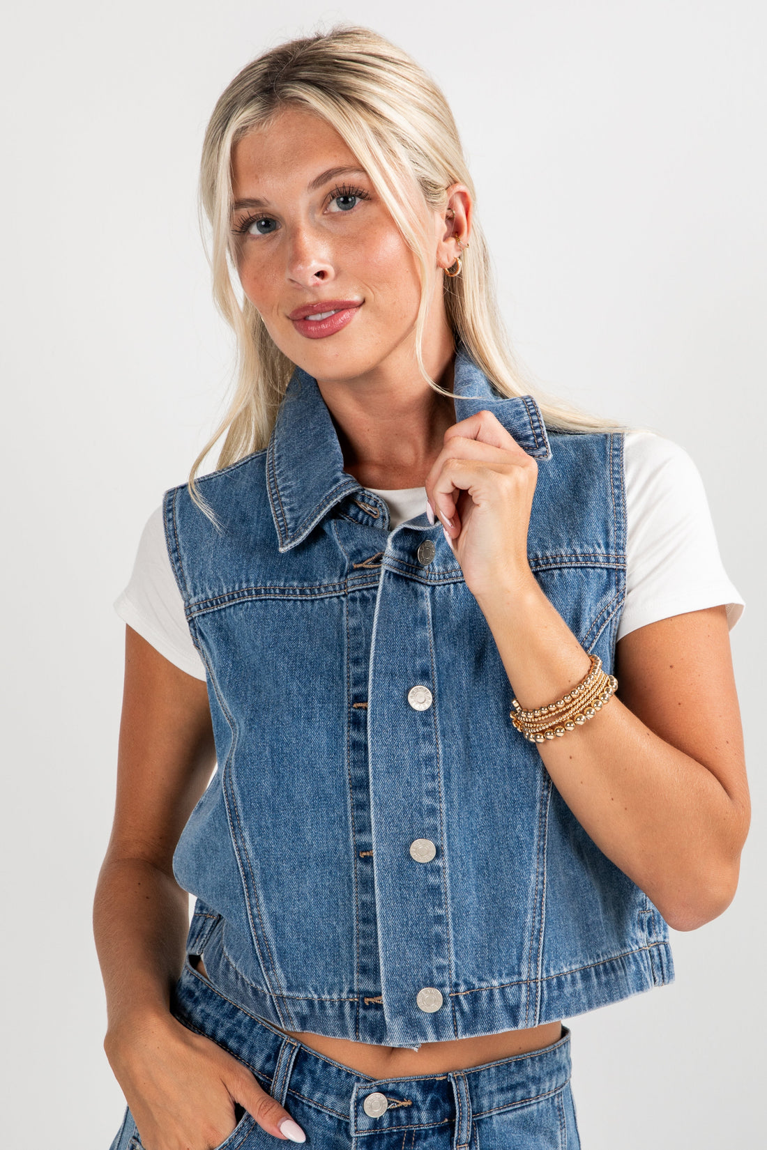 Woman wearing a denim vest over a white shirt on a plain background