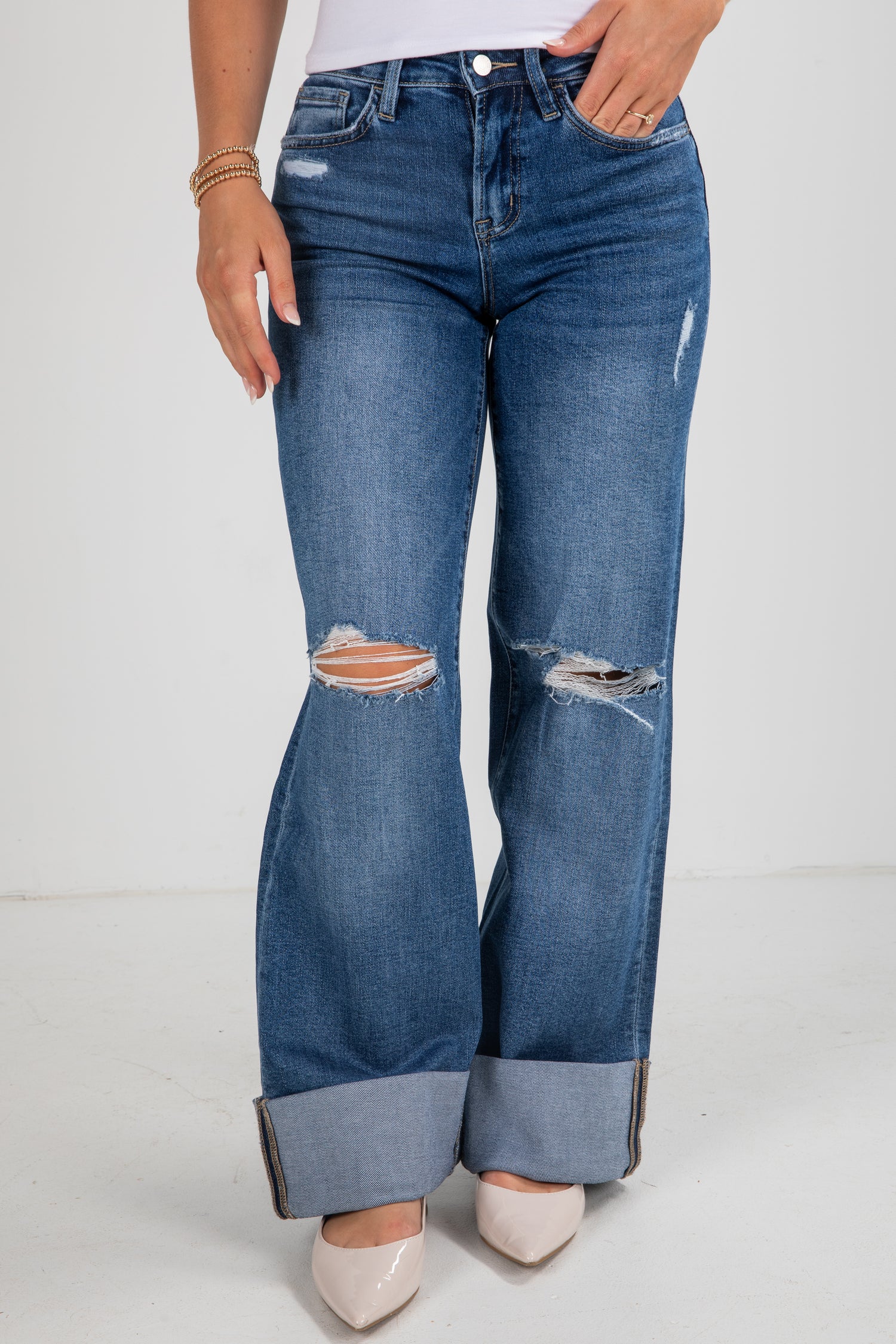 Person wearing blue jeans with distressed details on a white background