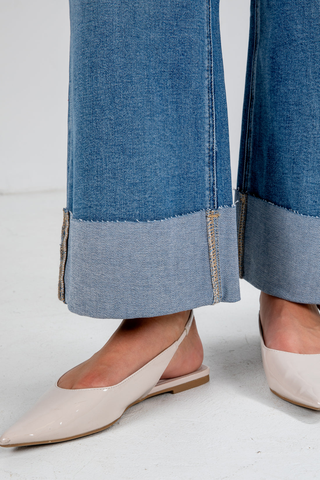 Close-up of blue jeans with a gray trim worn by a person wearing beige shoes on a white background