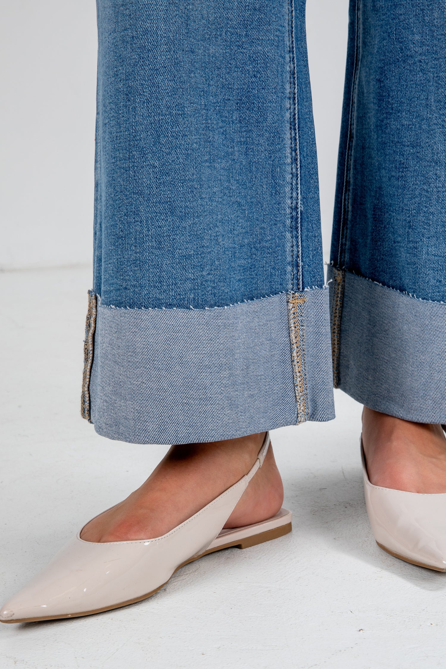 Close-up of blue jeans with a gray trim worn by a person wearing beige shoes on a white background