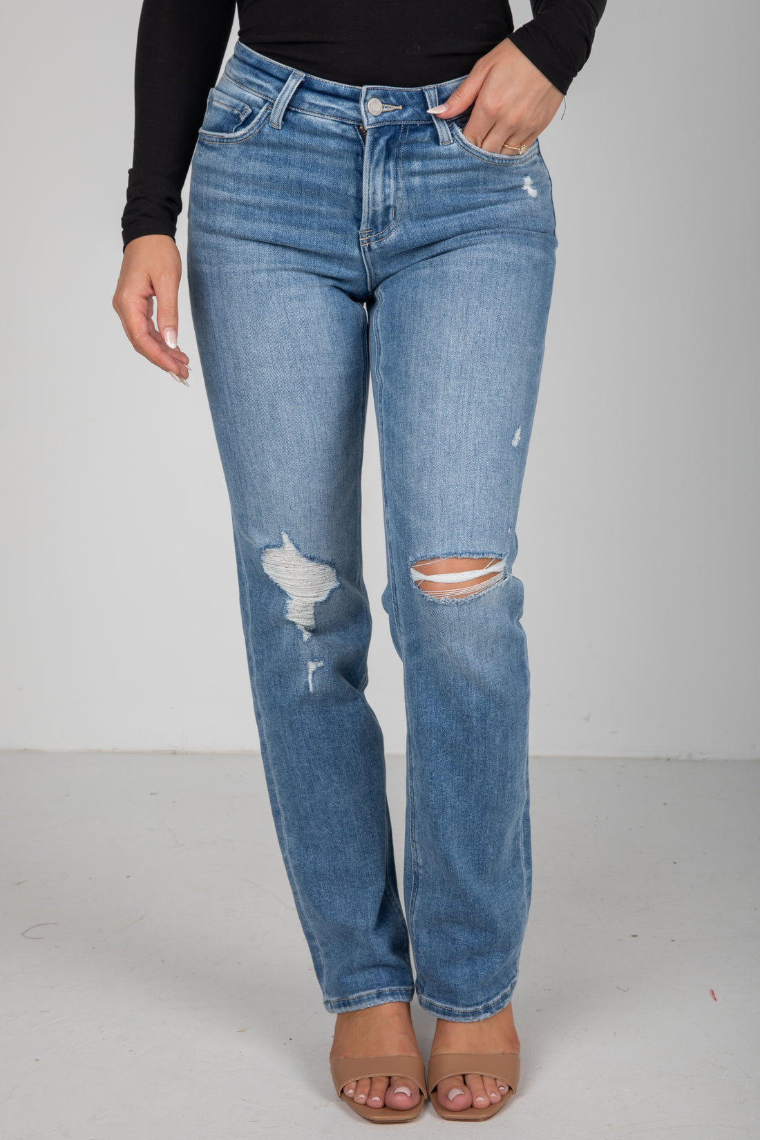 Person wearing distressed blue jeans on a plain background